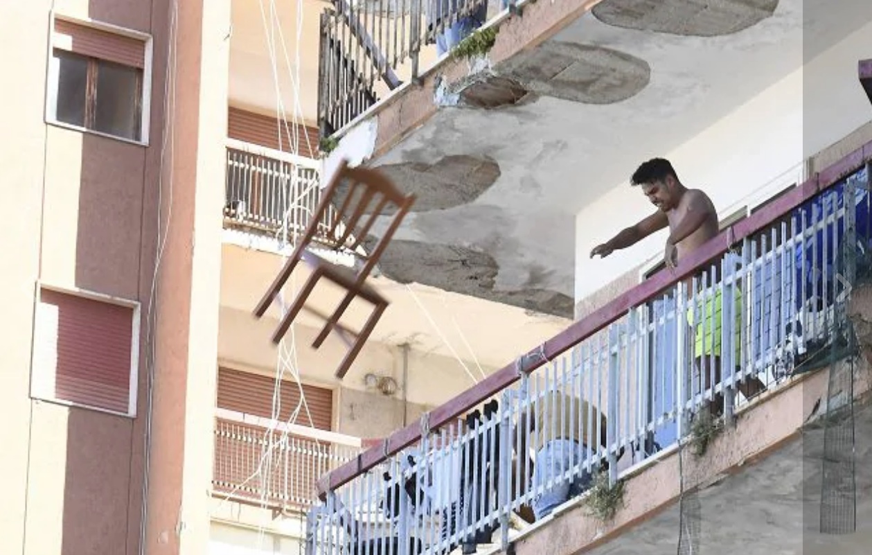 Un bulgaro che da un balcone del Palazzo ex Cirio di Mondragone lancia una sedia durante le proteste per il focolaio Covid (foto Ansa)